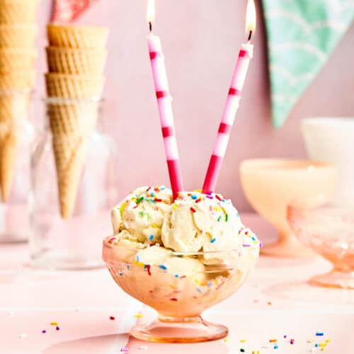 A bowl with several scoops of ice cream topped with sprinkles and two lit candles.
