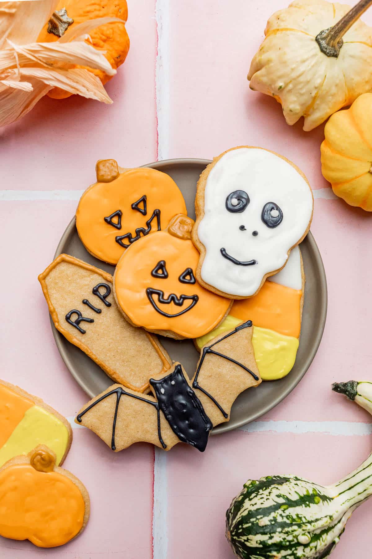 Several halloween-decorated sugar cookies on a plate with small pumpkins around.