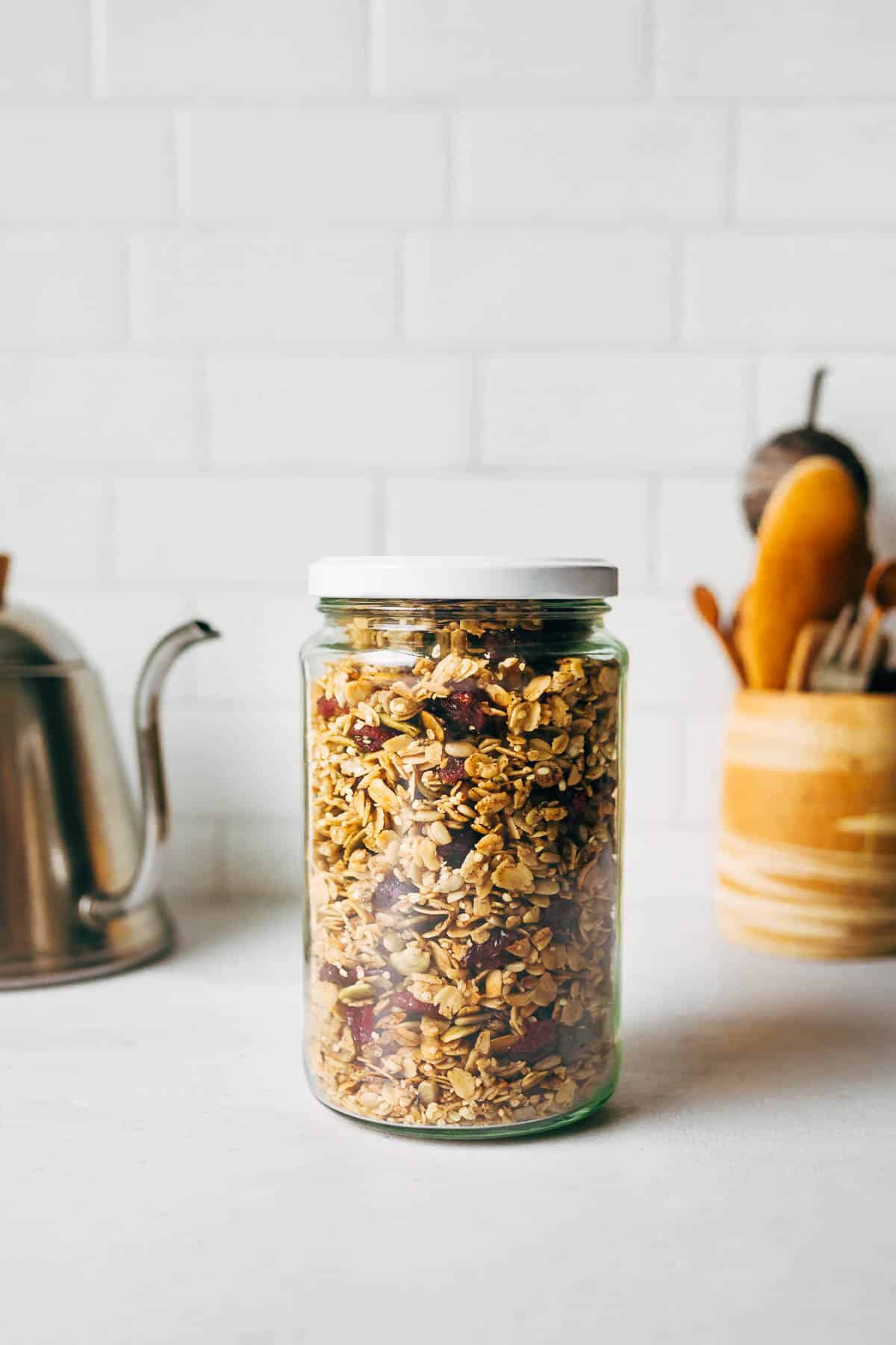 A glass jar of granola on the counter in a kitchen setting.