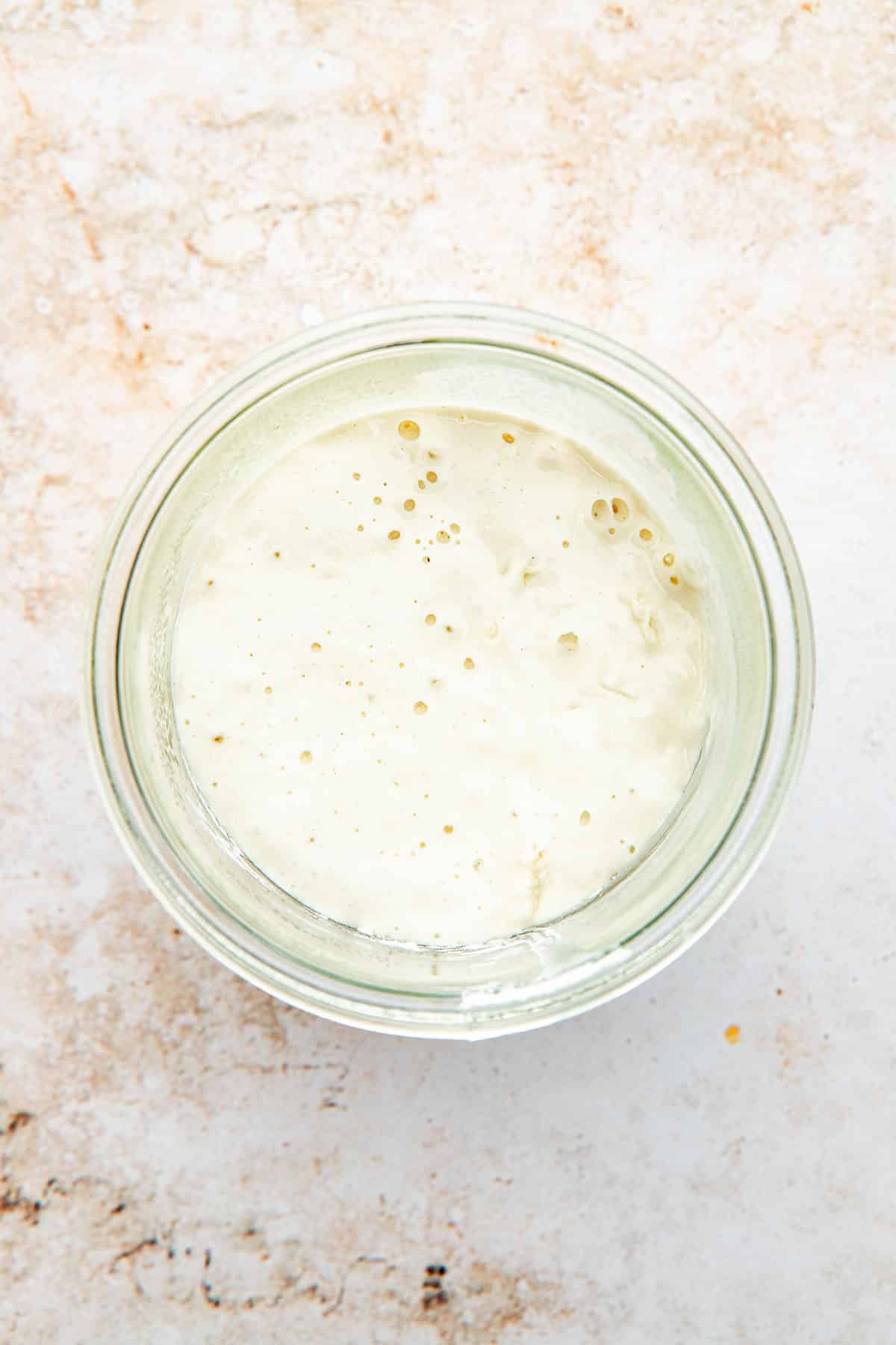 Top down view of a glass jar filled with active, bubbly sourdough starter.