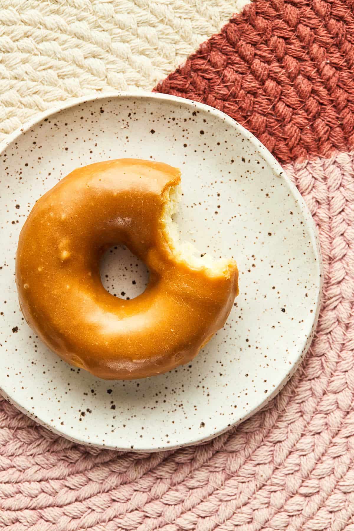 A single glazed donut on a small plate with a bite taken out of it.