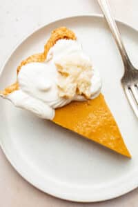 A slice of pumpkin pie on a plate, topped with cream and small cookie.