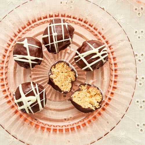 A pink glass plate topped with old-fashioned peanut butter balls with one of the balls cut in half to show the inside.
