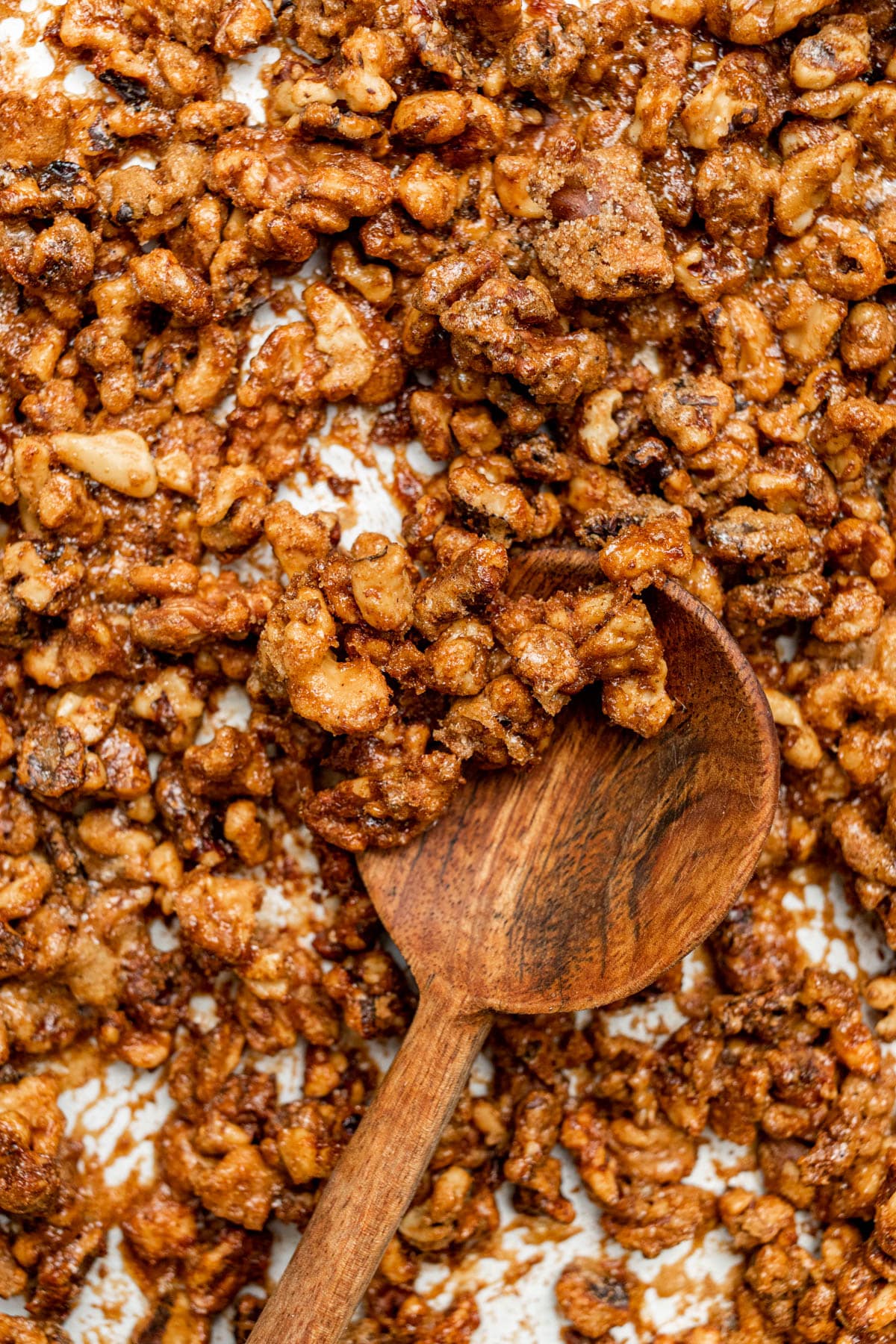 Candied walnuts on a baking sheet along with a decorative wooden spoon.