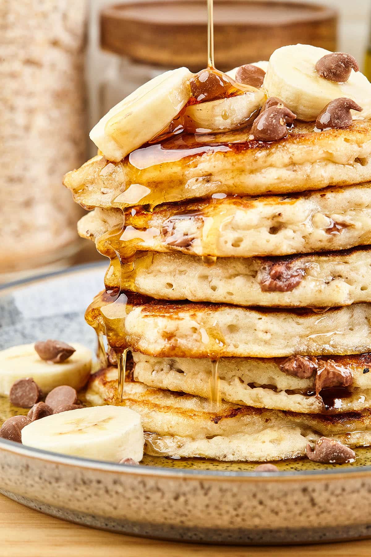 Close up of a stack of chocolate chip pancakes topped with banana slices and syrup.