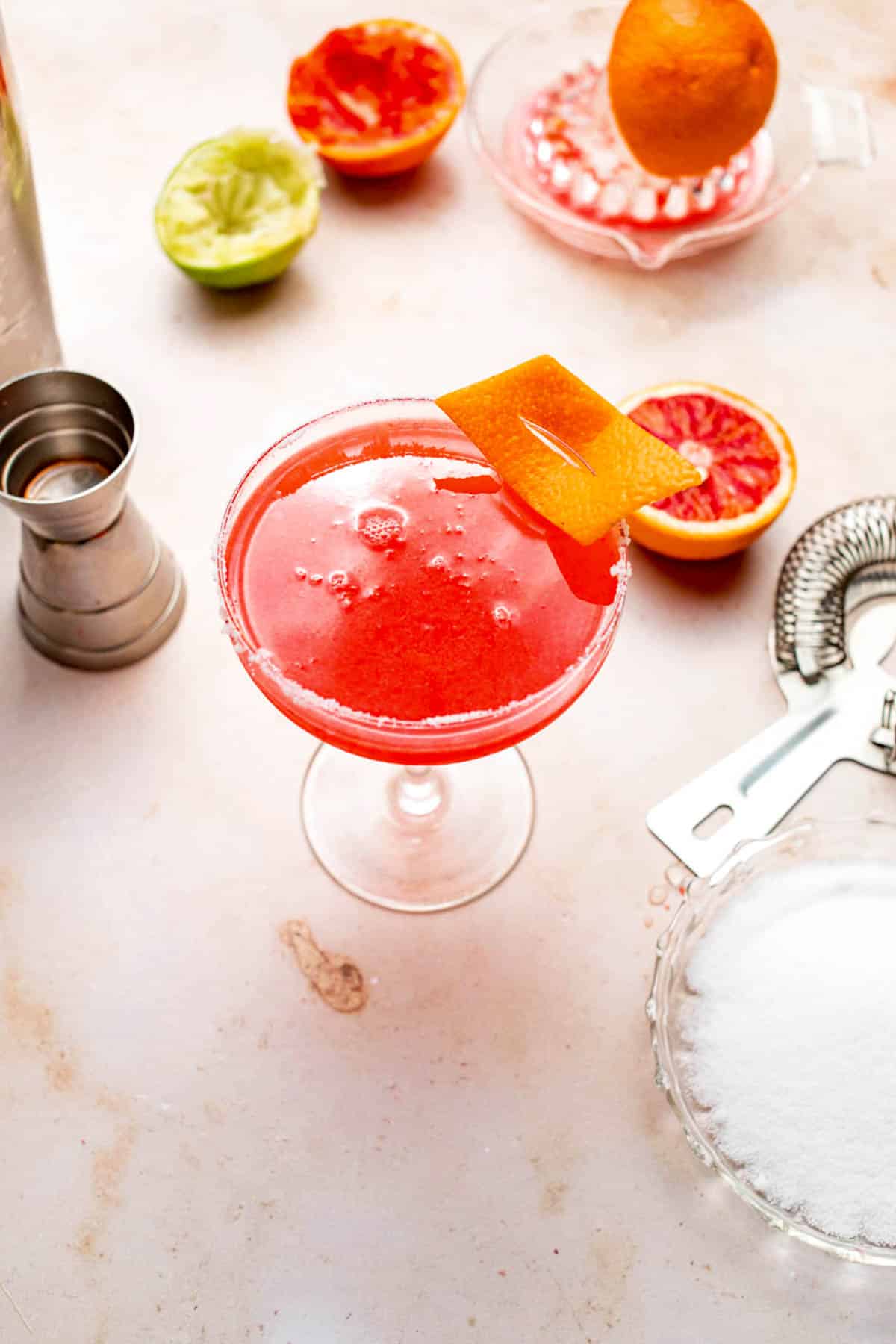 A pink-orange margarita in a cocktail glass with a slice of orange zest.