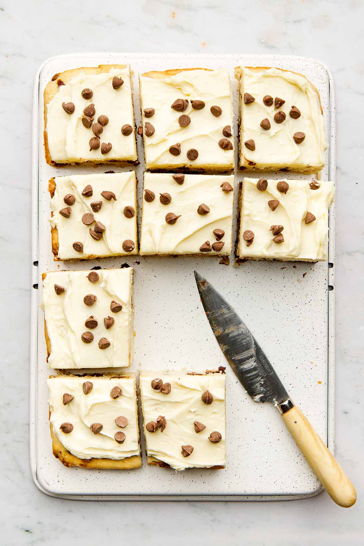 Chocolate chip-topped frosted cake cut into squares, top down view.
