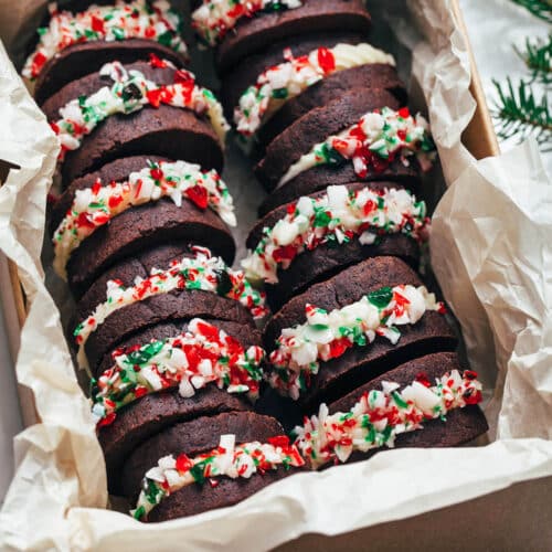 Several chocolate cookies sandwiched with buttercream and candy cane crumbs in a large tin.