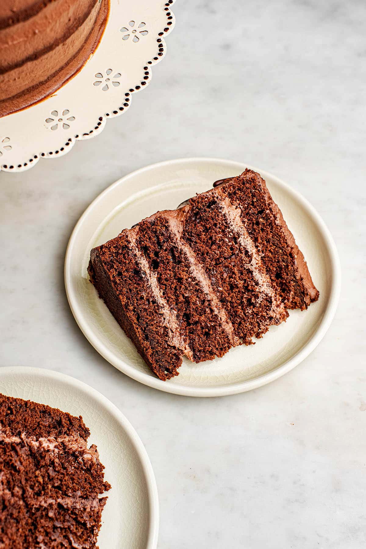 A slice of chocolate layer cake on a plate, with more cake nearby.
