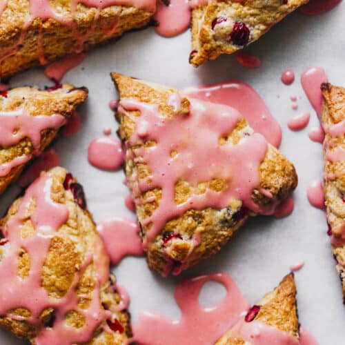 Several cranberry scones on a baking sheet topped with pink glaze.
