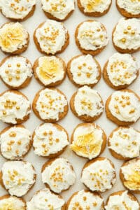 Dozens of small frosted cookies topped with gold sprinkles, top down view.