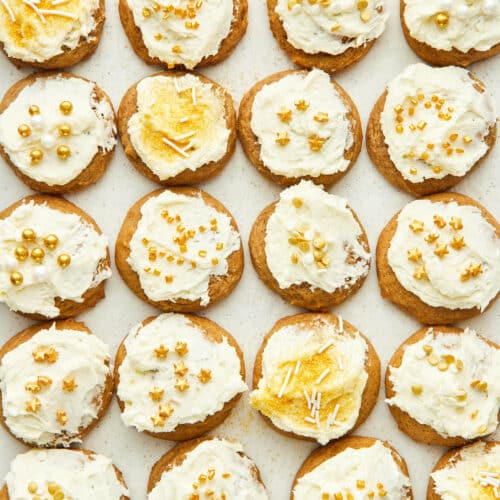 Dozens of small frosted cookies topped with gold sprinkles, top down view.