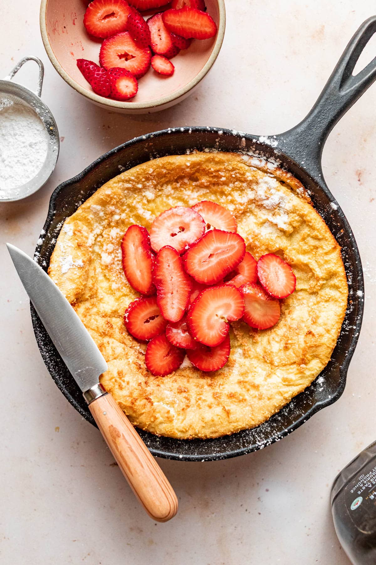A baked pancake in a cast-iron skillet topped with fresh sliced strawberries.