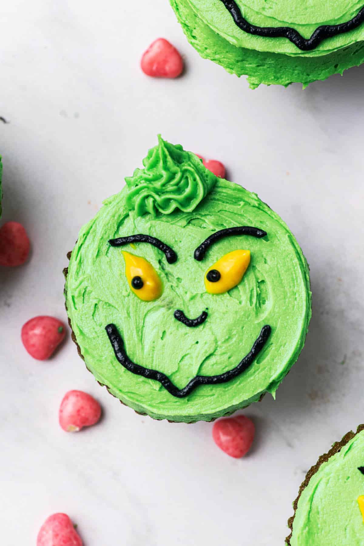 A shifty-looking grinch face made from buttercream on a cupcake base.
