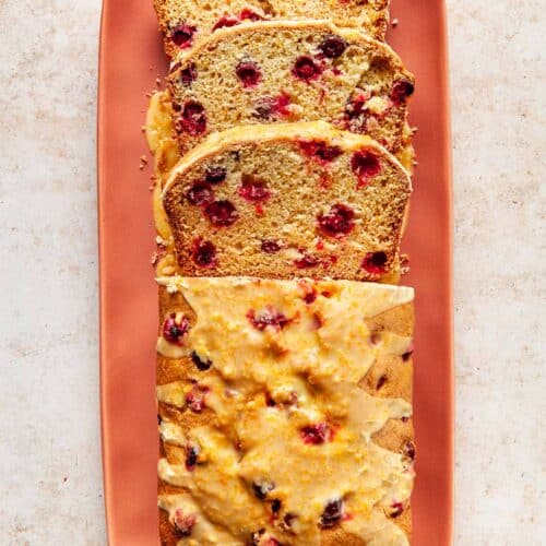 A loaf of cranberry bread on a serving dish with three slices cut.
