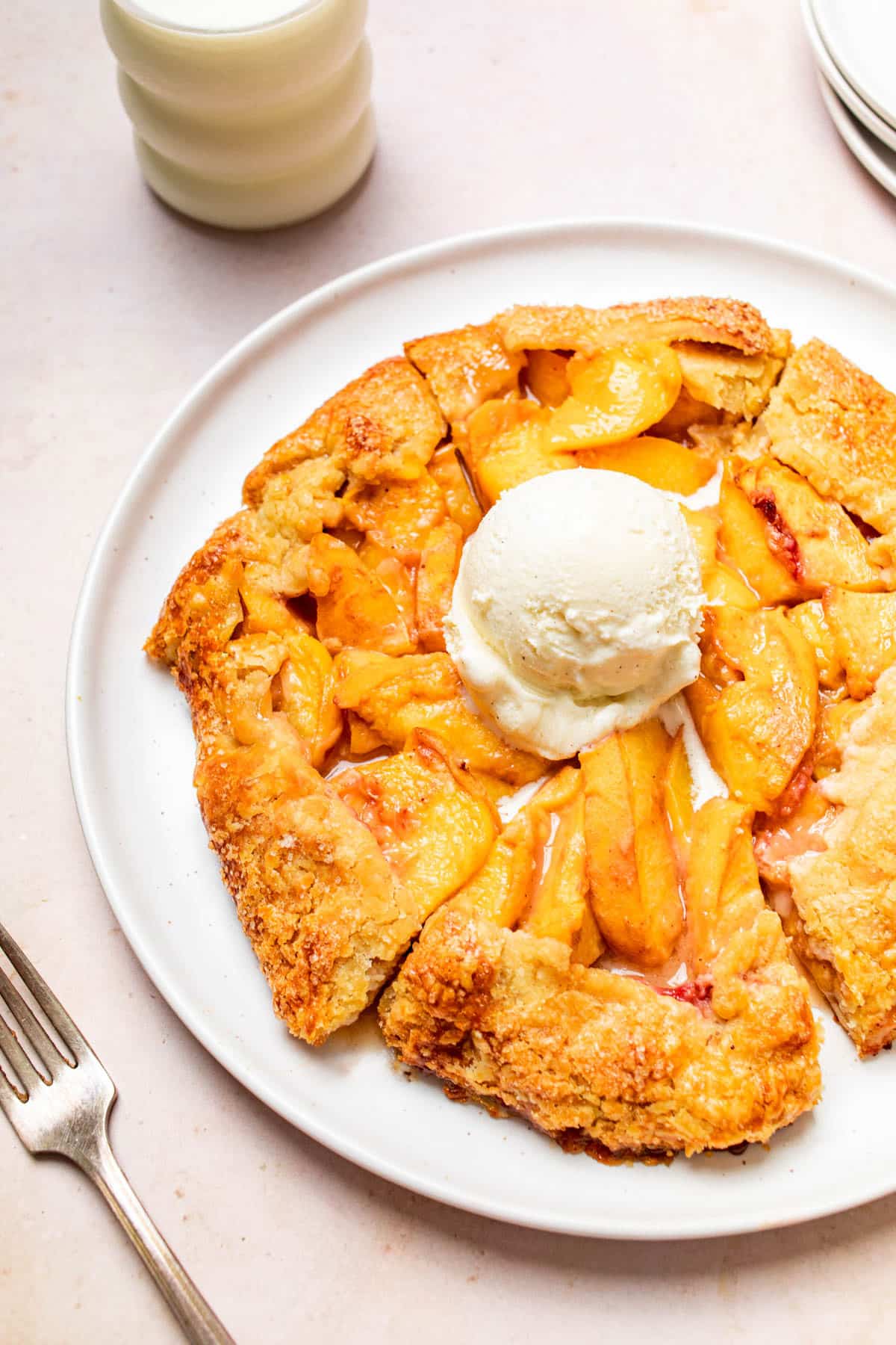Peach galette on a serving plate with a scoop of ice cream on top.