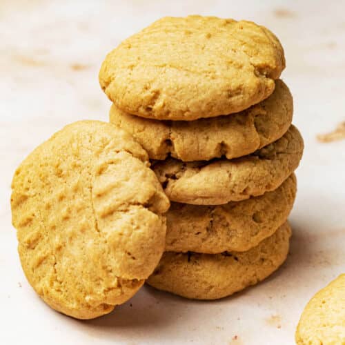 A stack of peanut butter cookies with one cookie leaning against it.