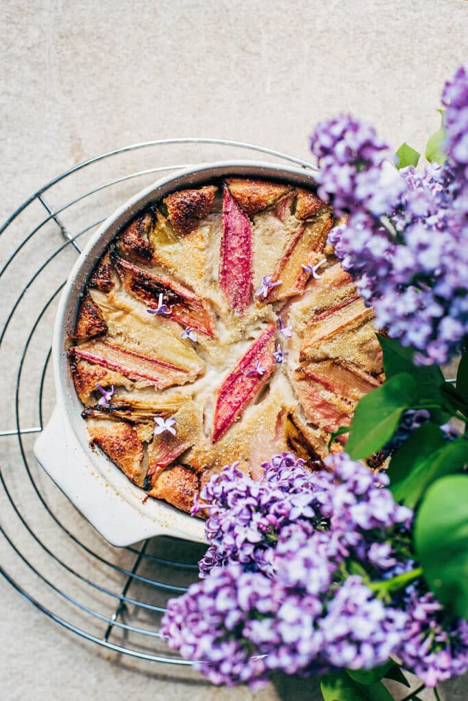 Top-down view of a rhubarb-topped clafoutis with lilacs around.