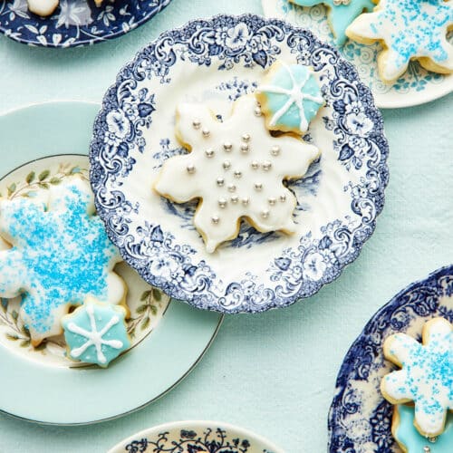 Snowflake cookies decorated with blue and white icing on blue and white plates.