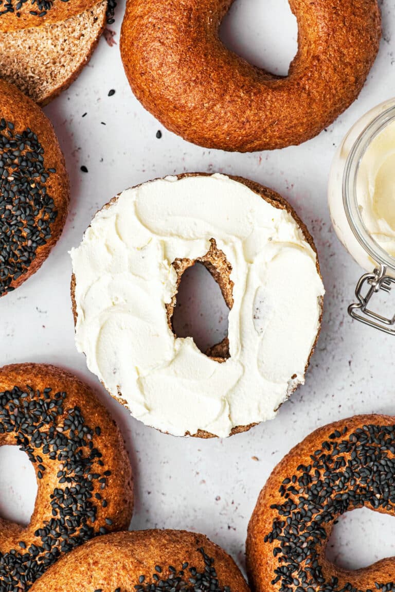 Whole wheat bagels, some topped with black sesame seeds, one halved with cream cheese.