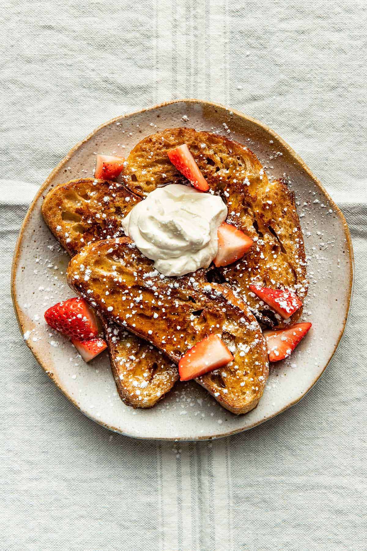 A plate with three slices of french toast topped with cream and strawberries.