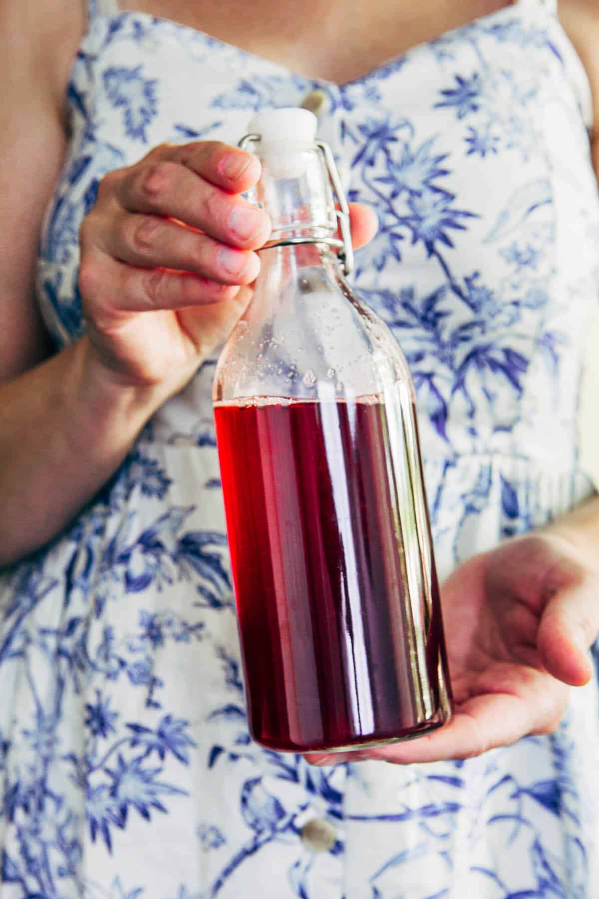 Woman holding a bottle of red syrup in front of herself.
