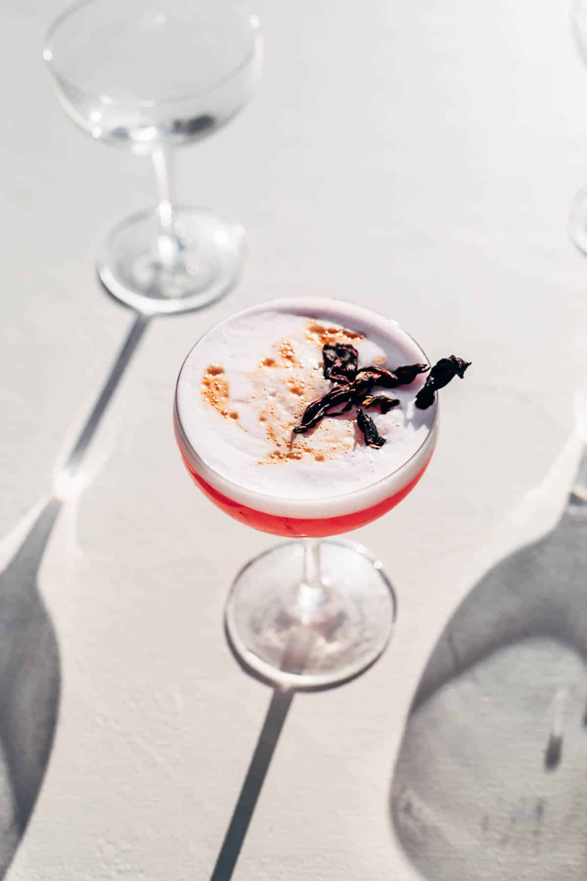 A pink cocktail topped with foam and dried hibiscus flowers.