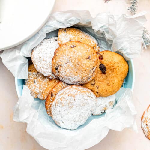 A tin filled with small cookies, some topped with icing sugar.