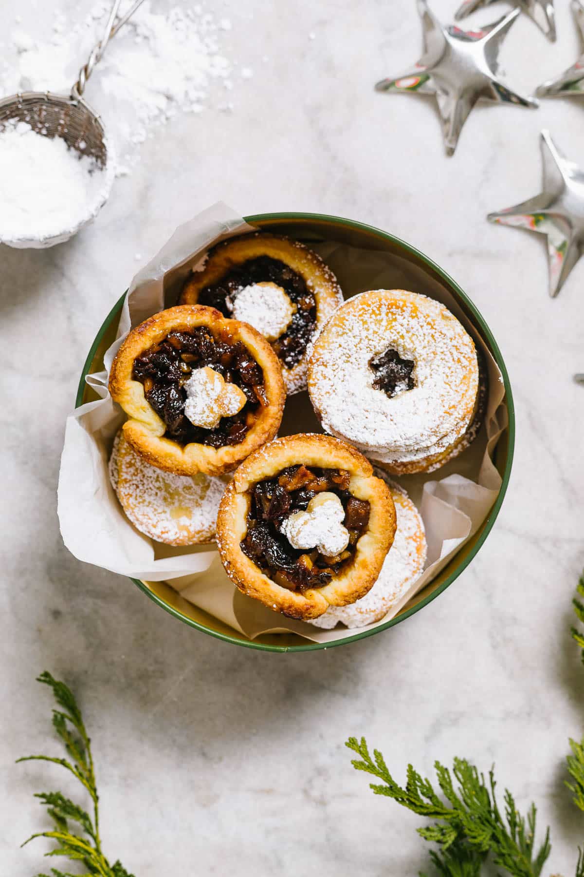 Mince tarts in a tin with holiday decorations around.