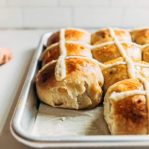 A pan of hot cross buns with one removed.