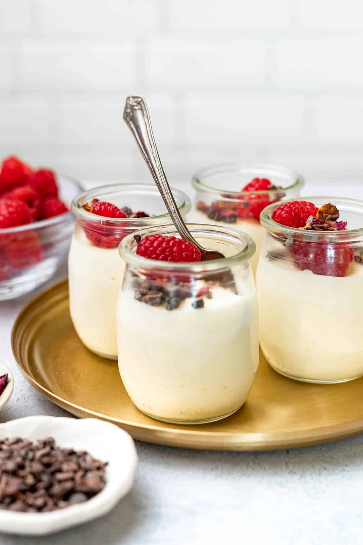 Four small glass cups of white chocolate mousse topped with raspberries.