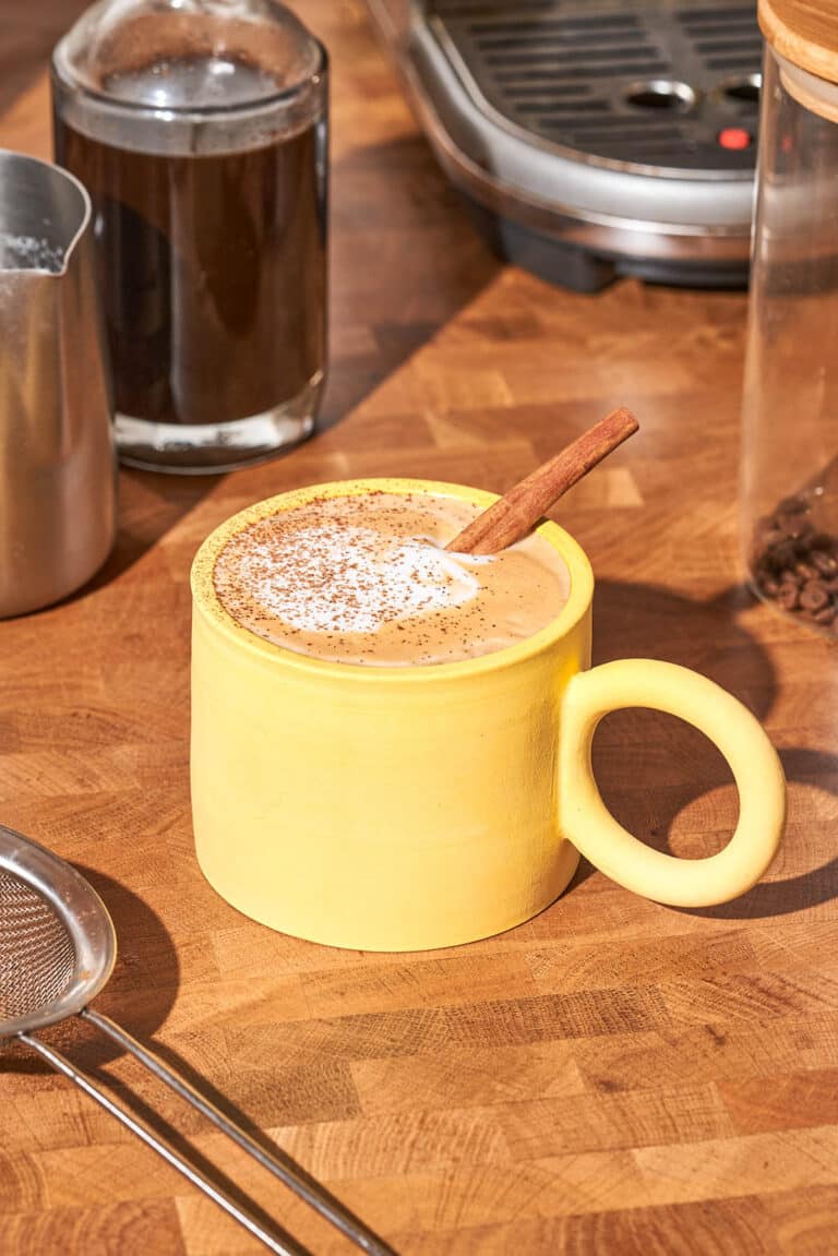A yellow mug filled with a latte topped with spiced and a cinnamon stick.