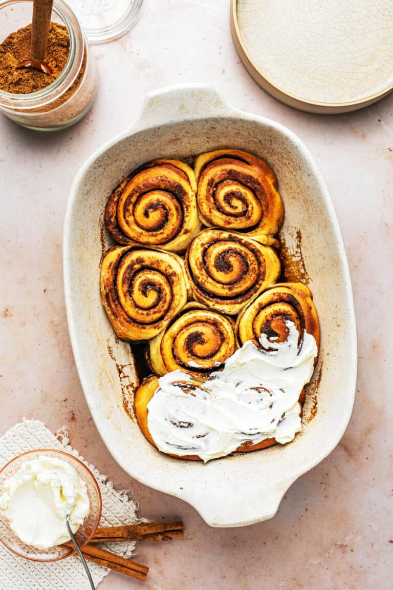 Top-down view of cinnamon rolls in a baking dish, partly frosted.