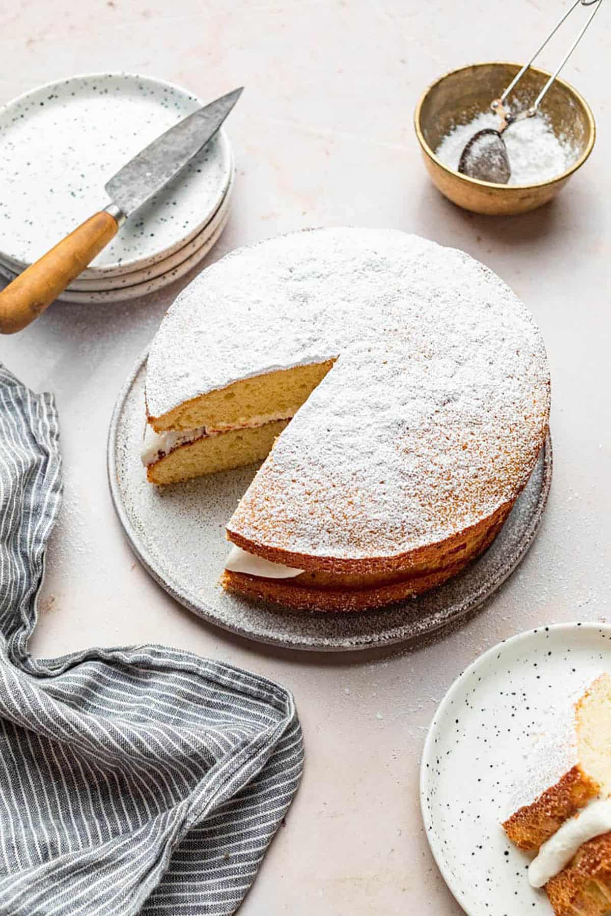 Layered white cake topped with icing sugar, one slice cut.