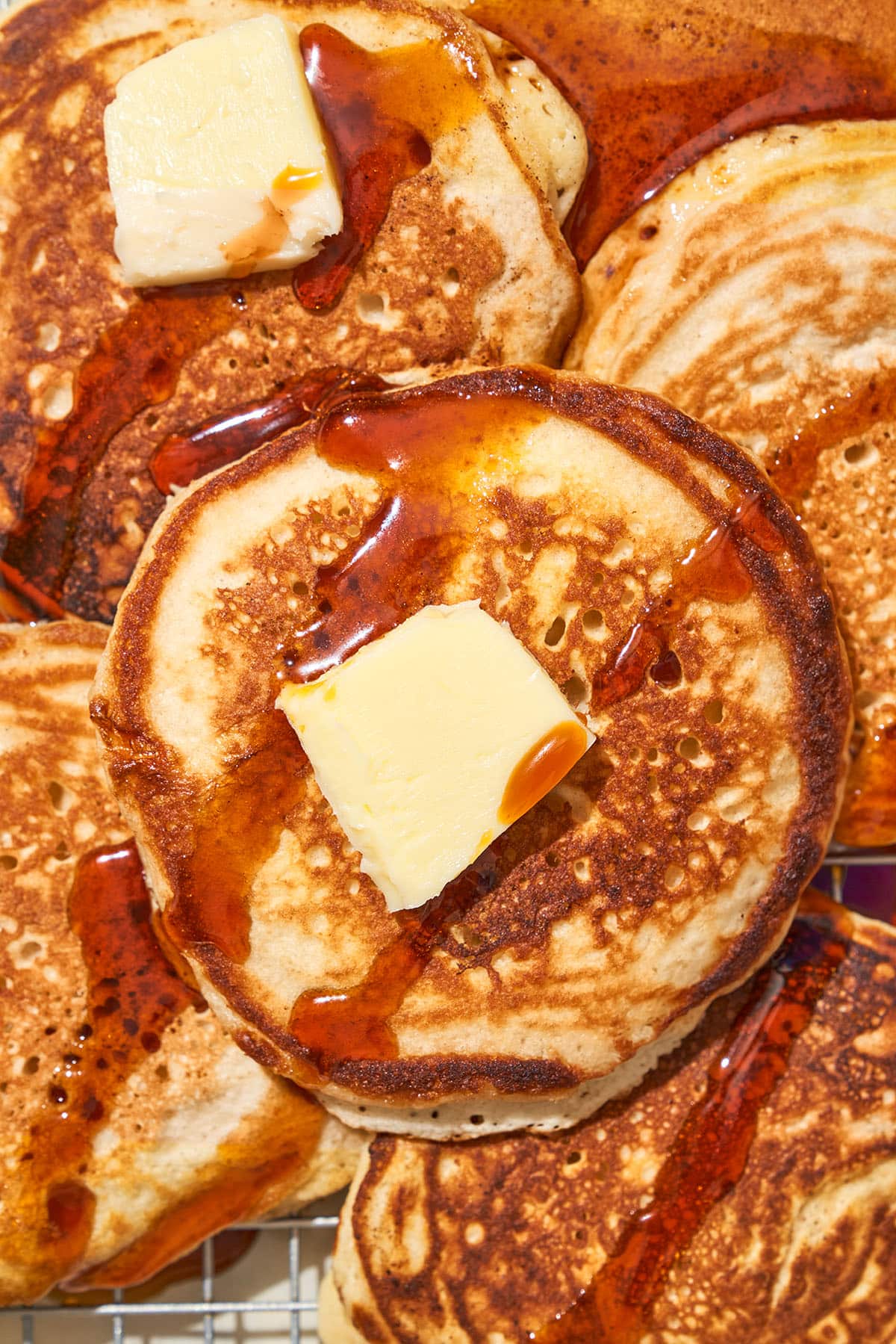 Top-down view of several pancakes topped with maple syrup and butter.
