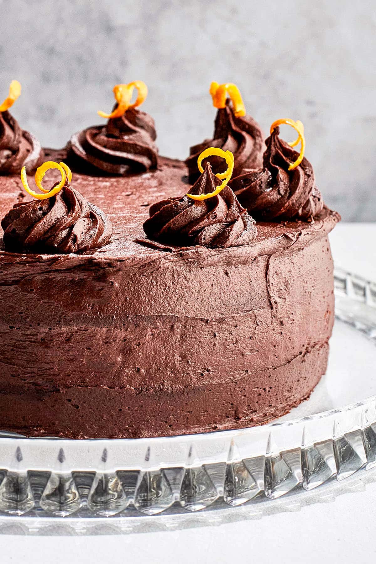 Close up of a chocolate frosted cake with frosting mounds and orange peel.