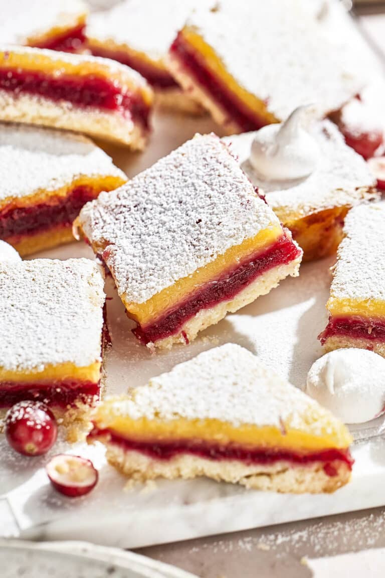 Icing sugar-topped cranberry and lemon layer bars on a white marble piece.