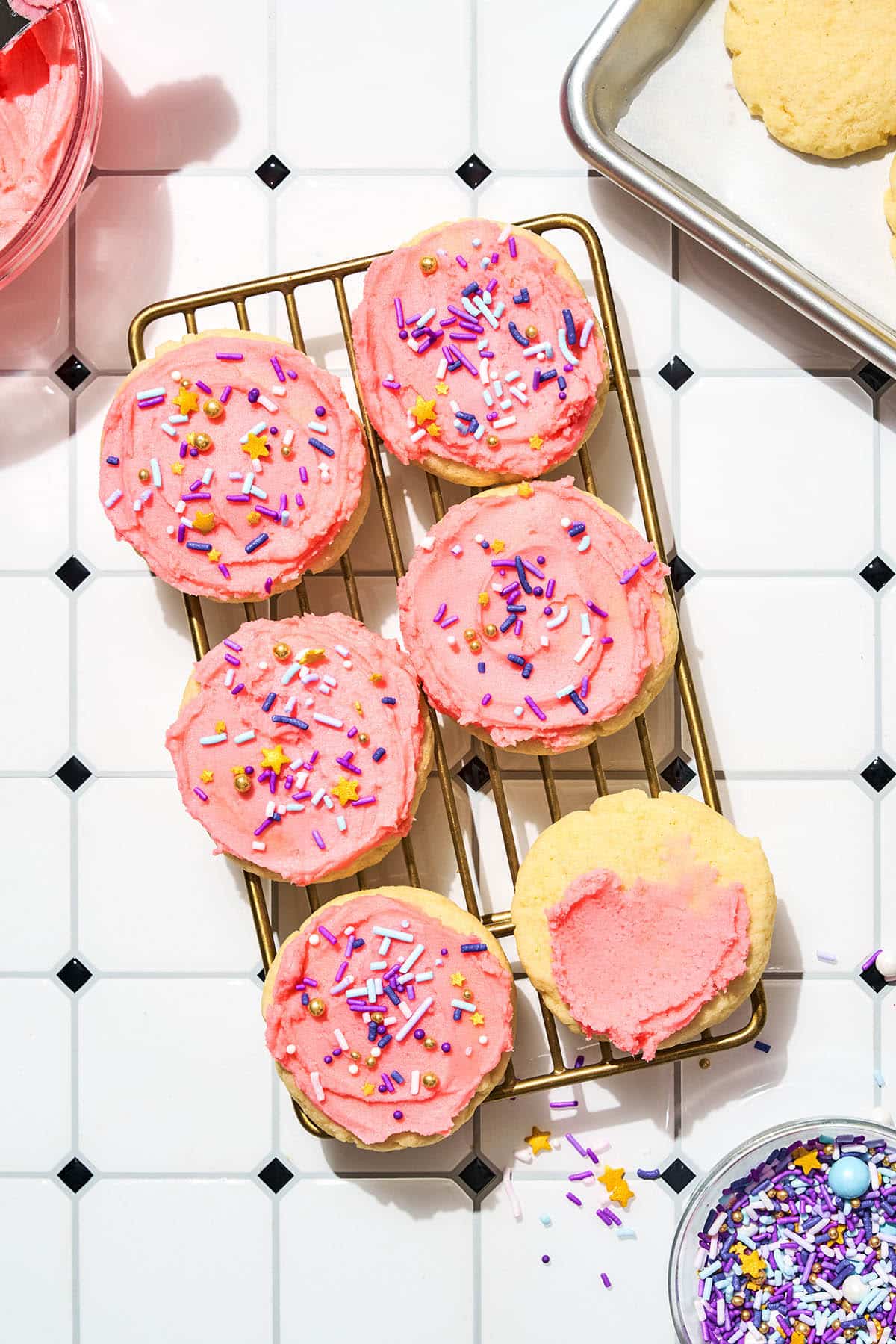 Cookies on a wire rack with pink frosting and sprinkles, top down view.