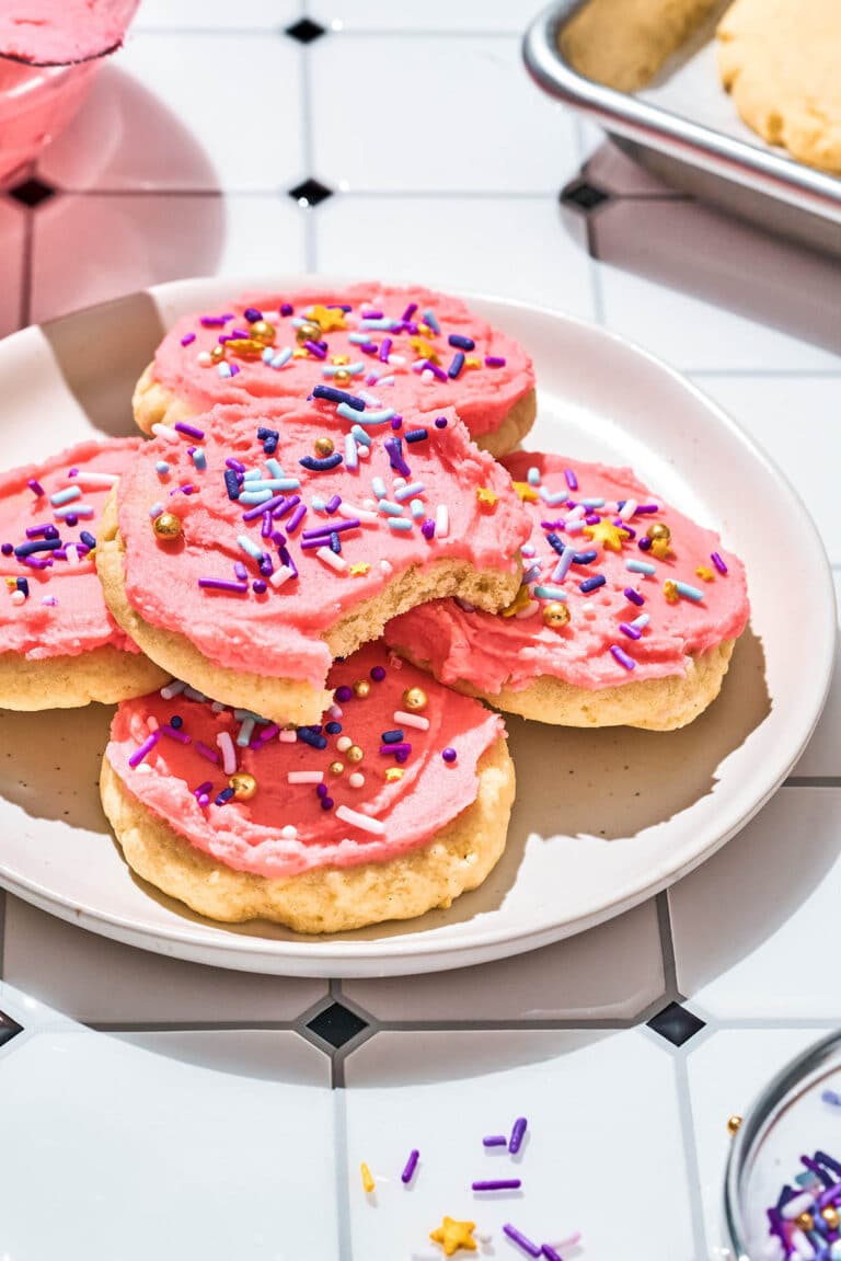 Several pink-frosted sugar cookies on a plate, topped with sprinkles.