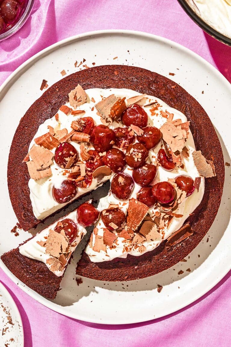 Top-down view of a chocolate cake topped with whipped cream, cherries, and chocolate shavings.
