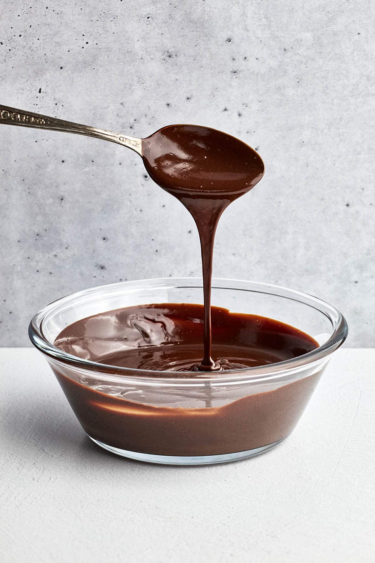 Ganache pouring from a tablespoon over a bowl full.