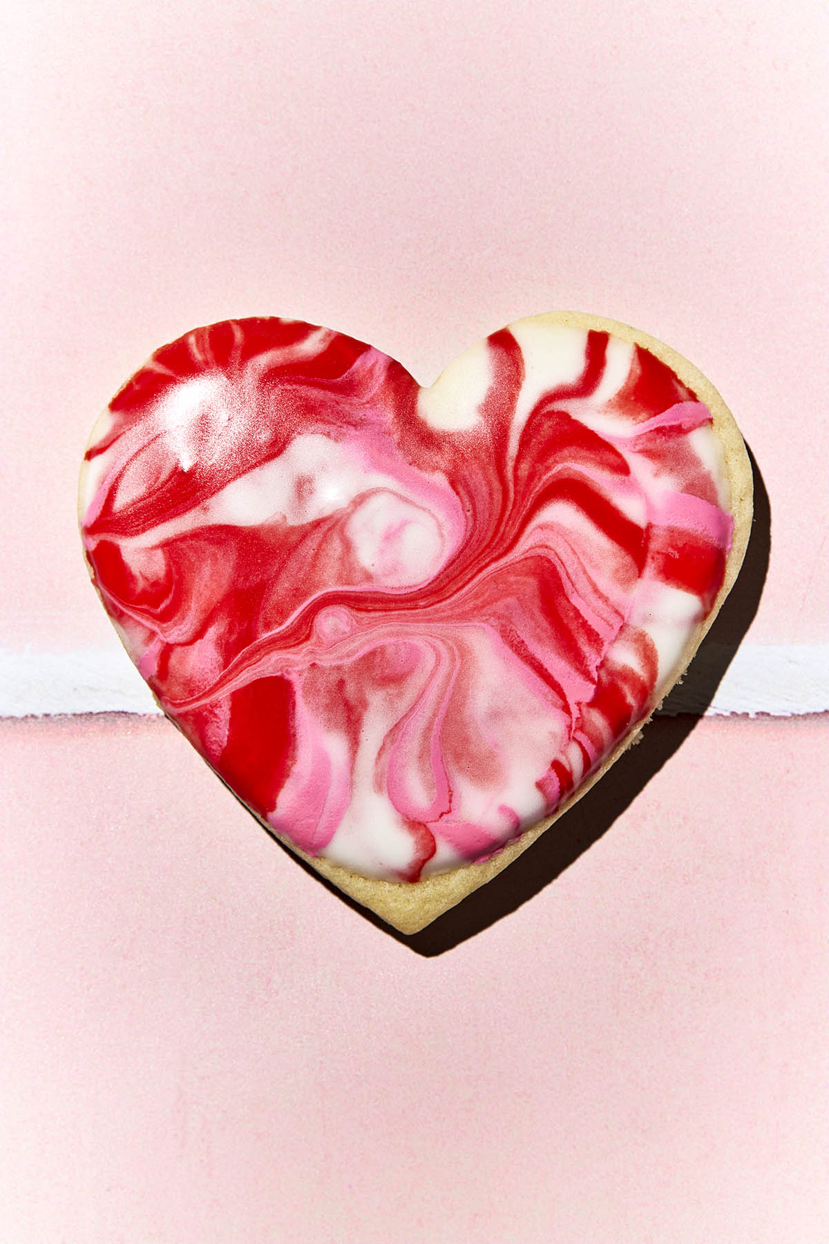 A heart-shaped cookie with marbled red, white, and pink icing.