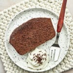 A slice of chocolate loaf cake on a plate with whipped cream.
