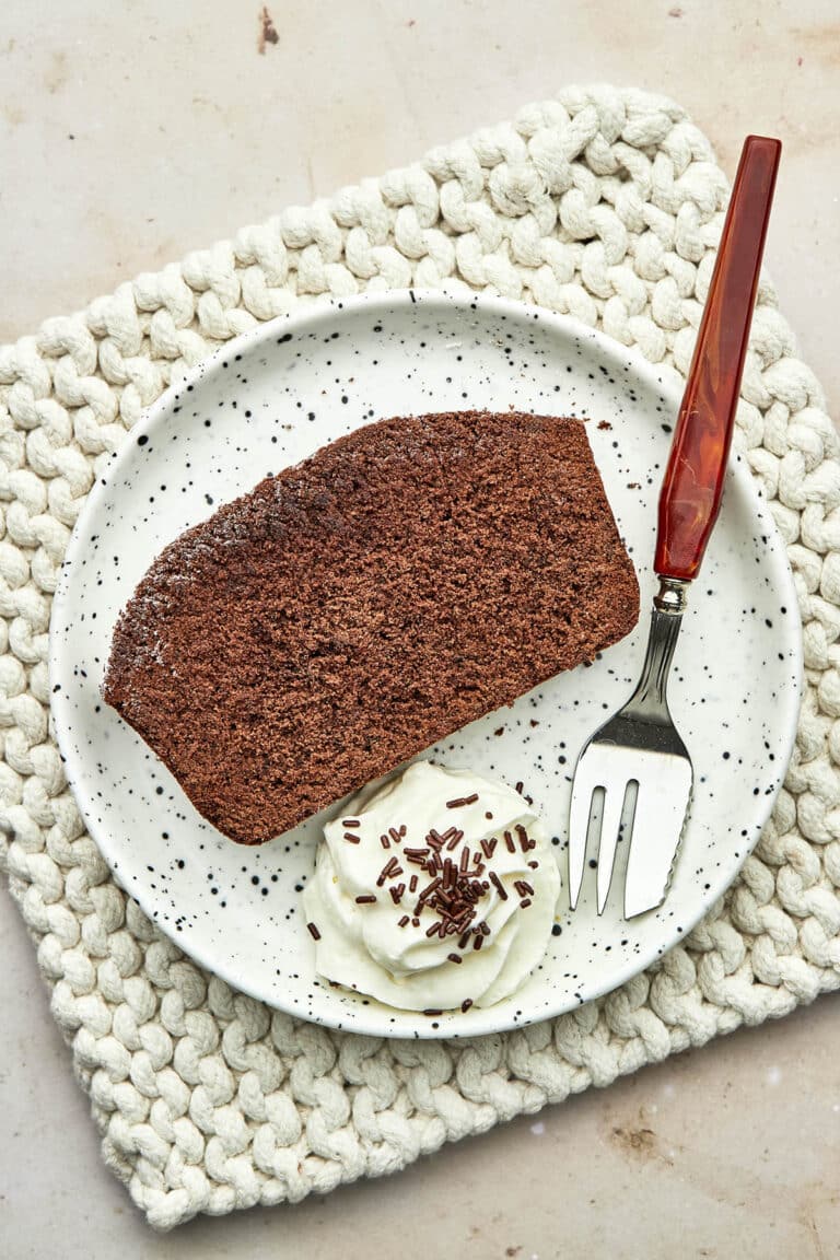 A slice of chocolate loaf cake on a plate with whipped cream.