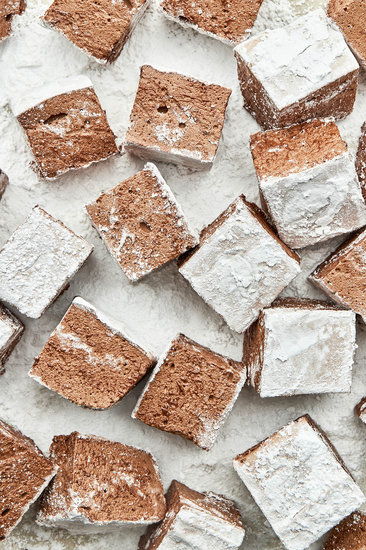 Several cocoa marshmallow squares sitting in powdered sugar.