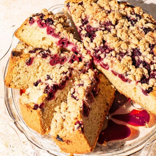 A large single-layer cake with cherries and a crumble topping on a glass cake stand.