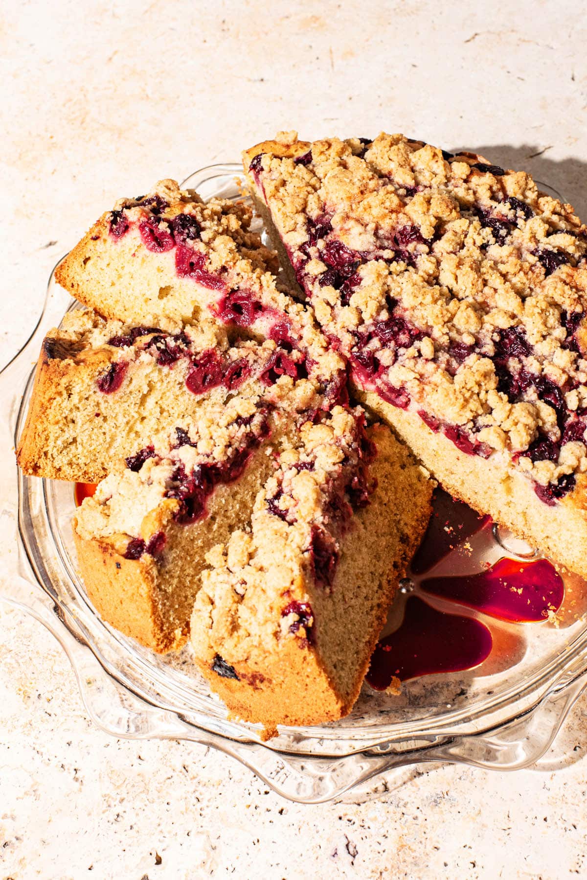 A large single-layer cake with cherries and a crumble topping on a glass cake stand.