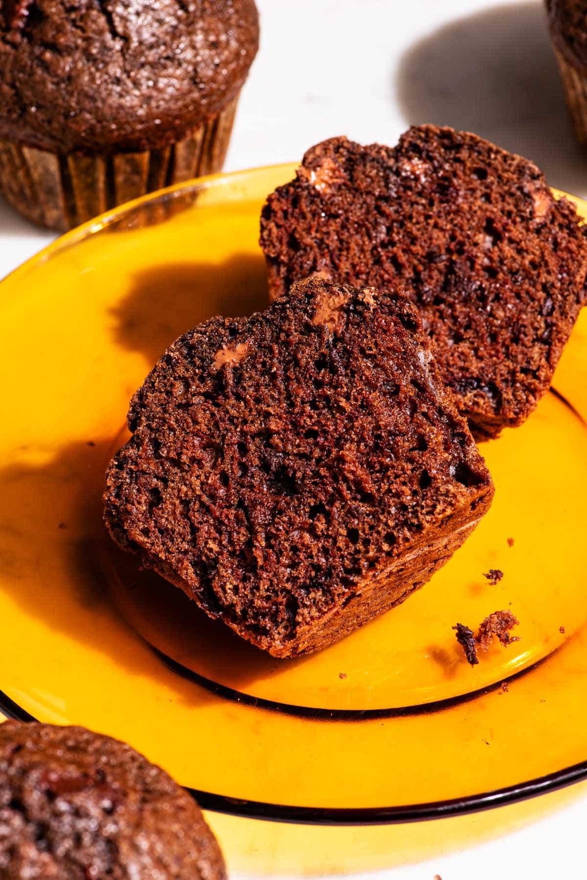 Chocolate muffin sliced in half on an orange glass plate.