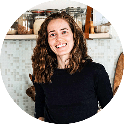 Smiling woman with shoulder length wavy hair standing in front of a kitchen counter.