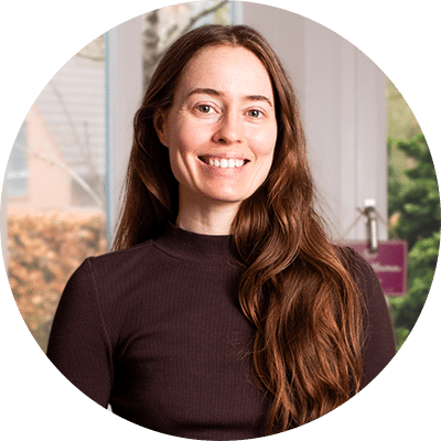 Woman smiling, with long brown hair in a dark brown shirt.